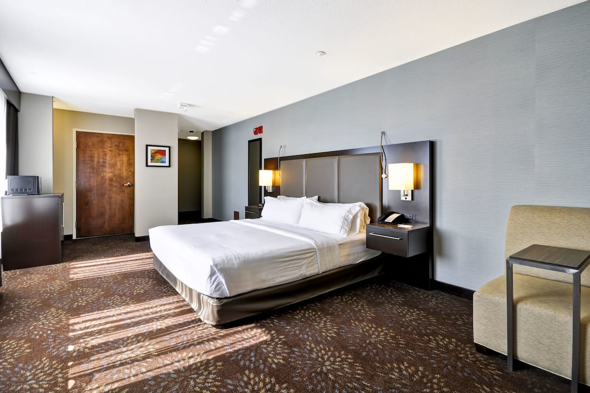 A hotel room with a large bed, bedside lamps, a desk, and a chair.