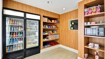 A well-stocked snack and beverage refrigerator, a microwave, and a shelf with branded mugs.