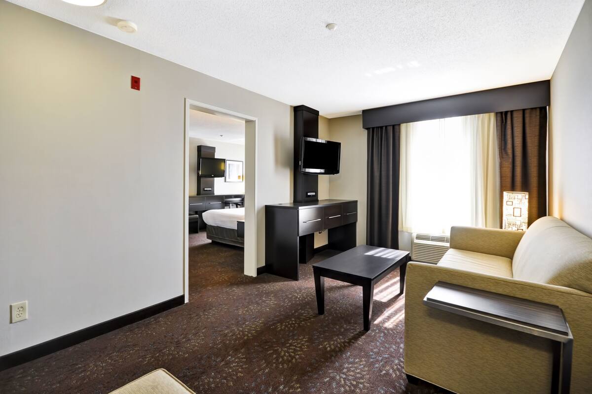 A hotel room with a bed, a TV, a sofa, a small table, and a window with curtains.