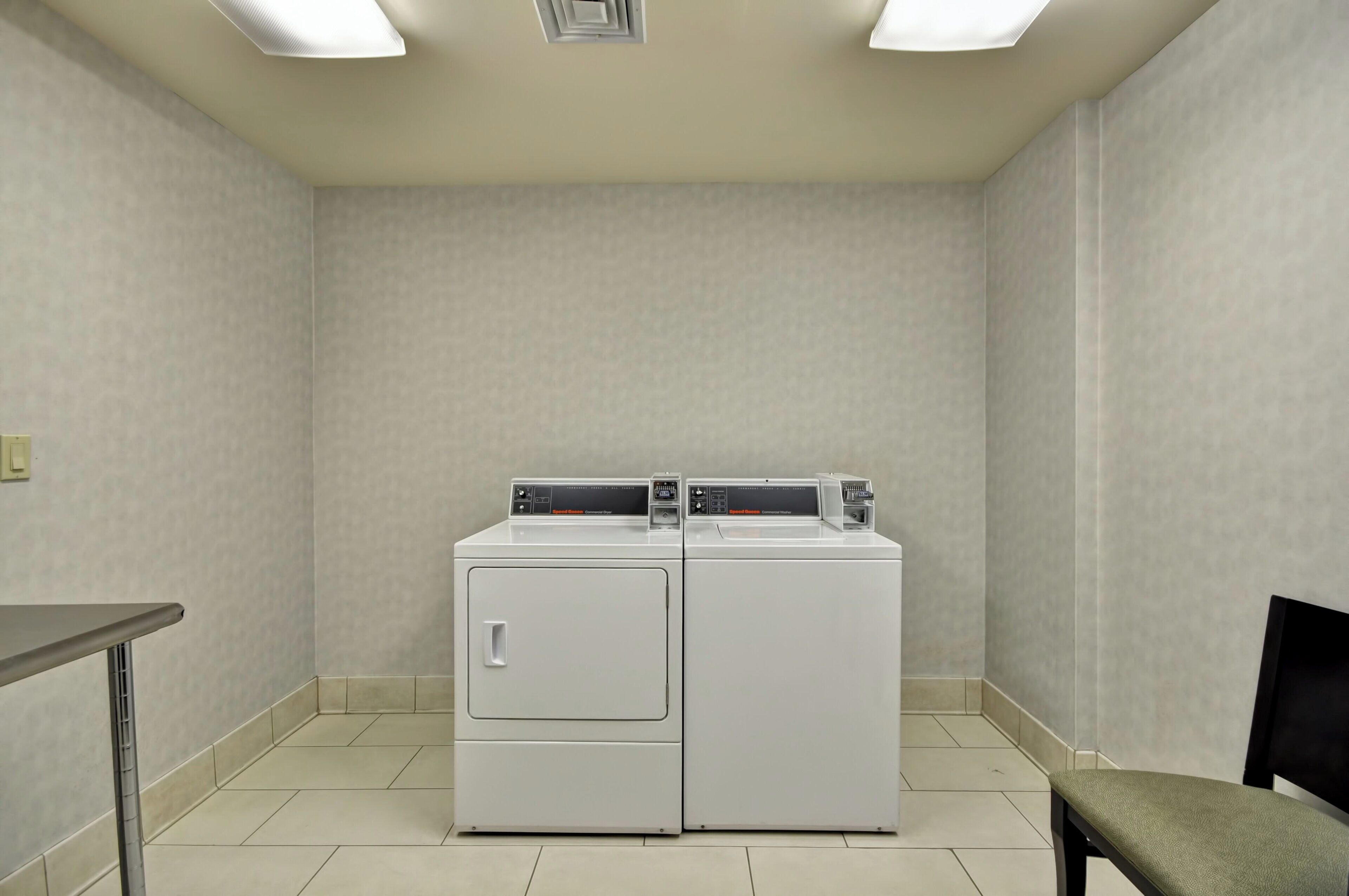 A laundry room with two stacked washers and dryers, a bench, and a table.