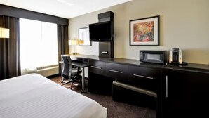 A hotel room with a bed, desk, chair, television, microwave, and artwork on the wall. - Holiday Inn Express Romulus / Detroit Airport by IHG (Romulus)