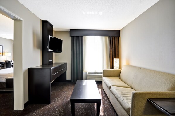 A hotel room with a bed, a TV, a desk, a sofa, and a window with curtains. - Holiday Inn Express Romulus / Detroit Airport by IHG (Romulus)