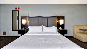 A hotel room with a large bed, two bedside tables with lamps, a chair, and a mirror on the wall. - Holiday Inn Express Romulus / Detroit Airport by IHG (Romulus)