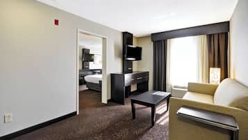 A hotel room with a bed, a desk, a television, a sofa, and a window with curtains.