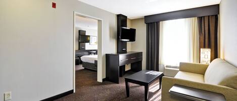 A hotel room with a bed, a desk, a television, a sofa, and a window with curtains.