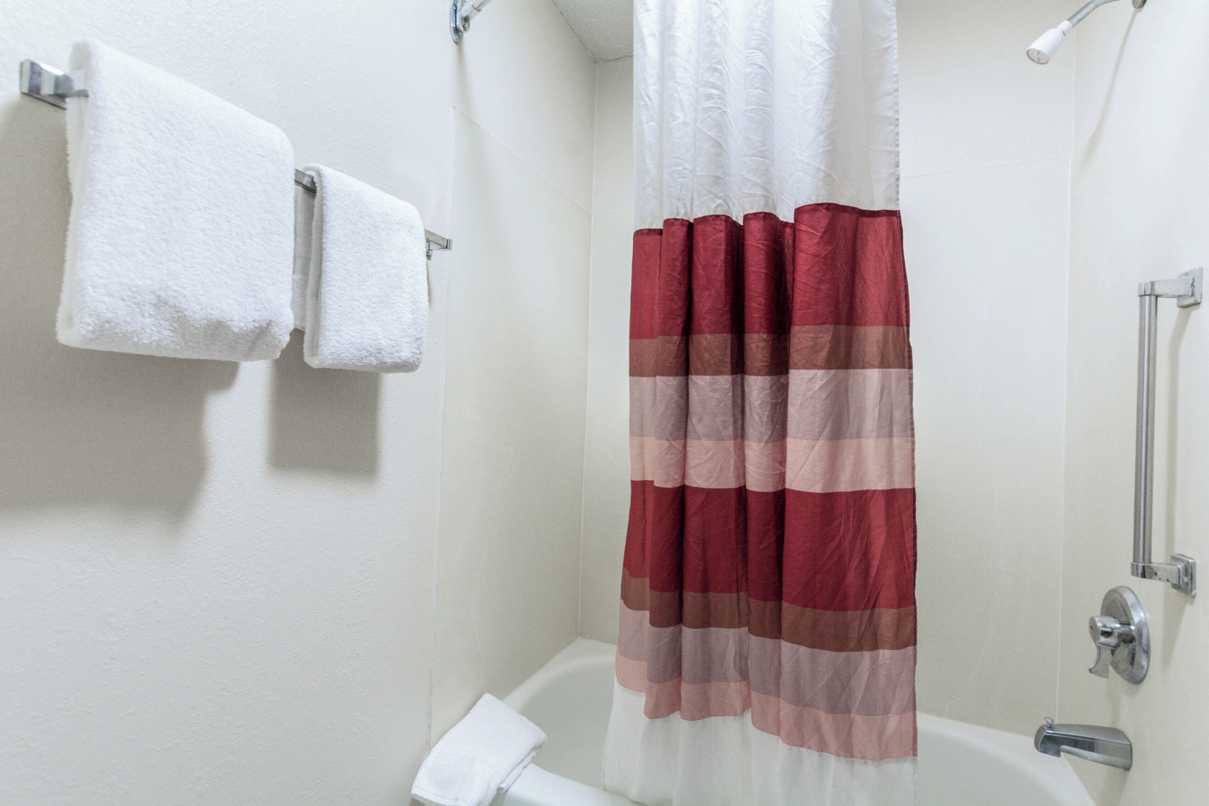 Un baño con una bañera blanca, un cortinón de ducha y dos toallas blancas colgadas en un perchero.