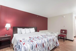 Una habitación de hotel con cama, mesita de noche, silla, bañera y espejo.