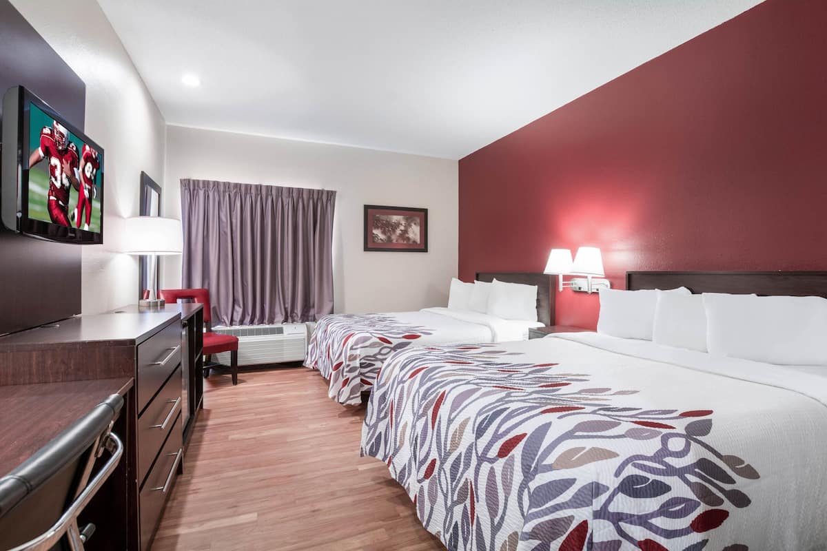 Une chambre d’hôtel comprenant un lit, un bureau, une télévision, une fenêtre avec des rideaux et un tableau accroché au mur.