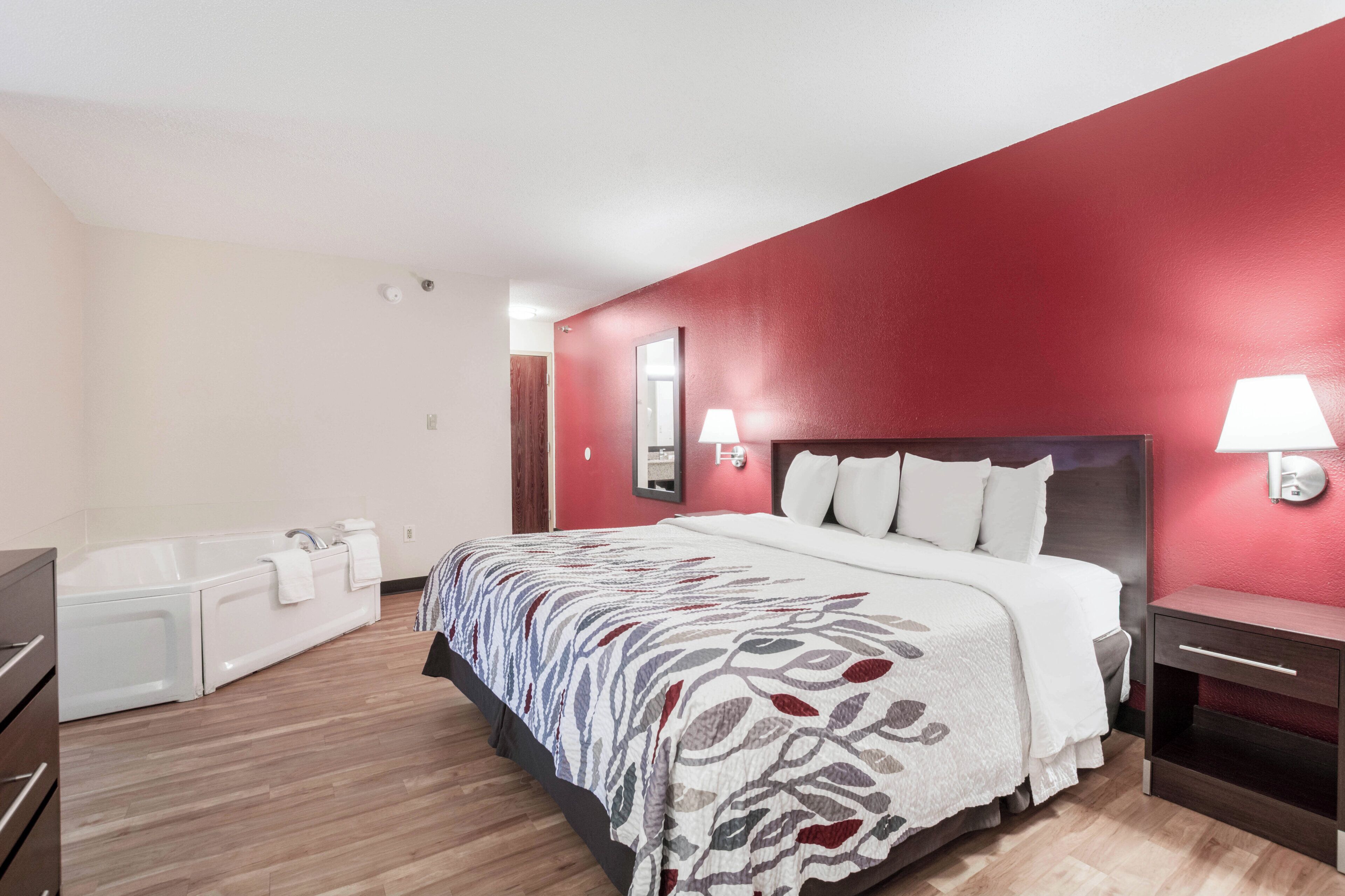 A hotel room with a large bed, a bathtub, and a red accent wall.