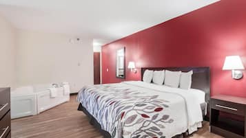 A hotel room with a large bed, a bathtub, and a red accent wall.