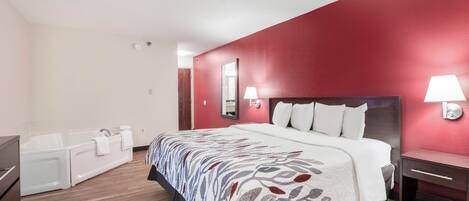 Quarto de hotel com cama grande, banheira e parede com detalhes em vermelho.
