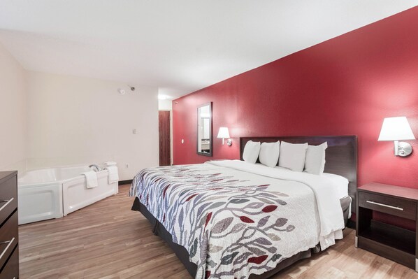 Habitación de hotel con una cama grande, una bañera y una pared de acento roja.