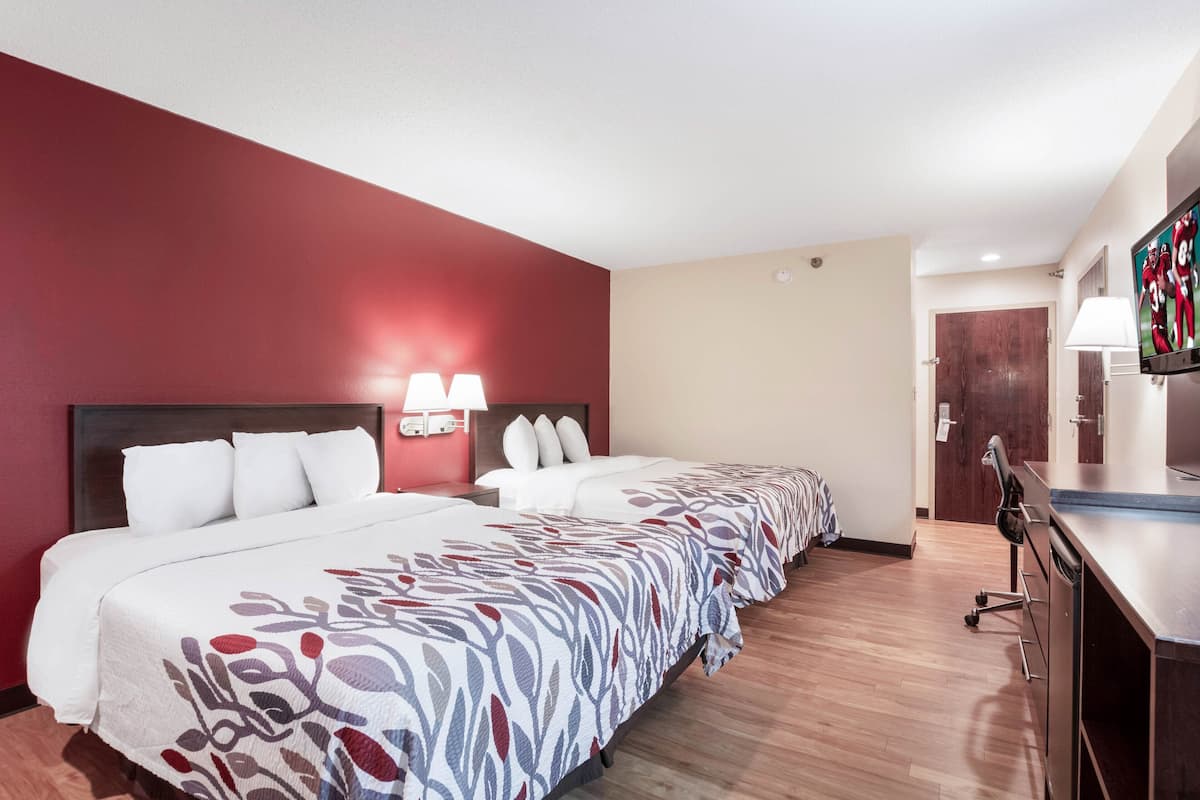 Une chambre d’hôtel avec deux lits, un bureau, une télévision et un mur d’accent rouge.