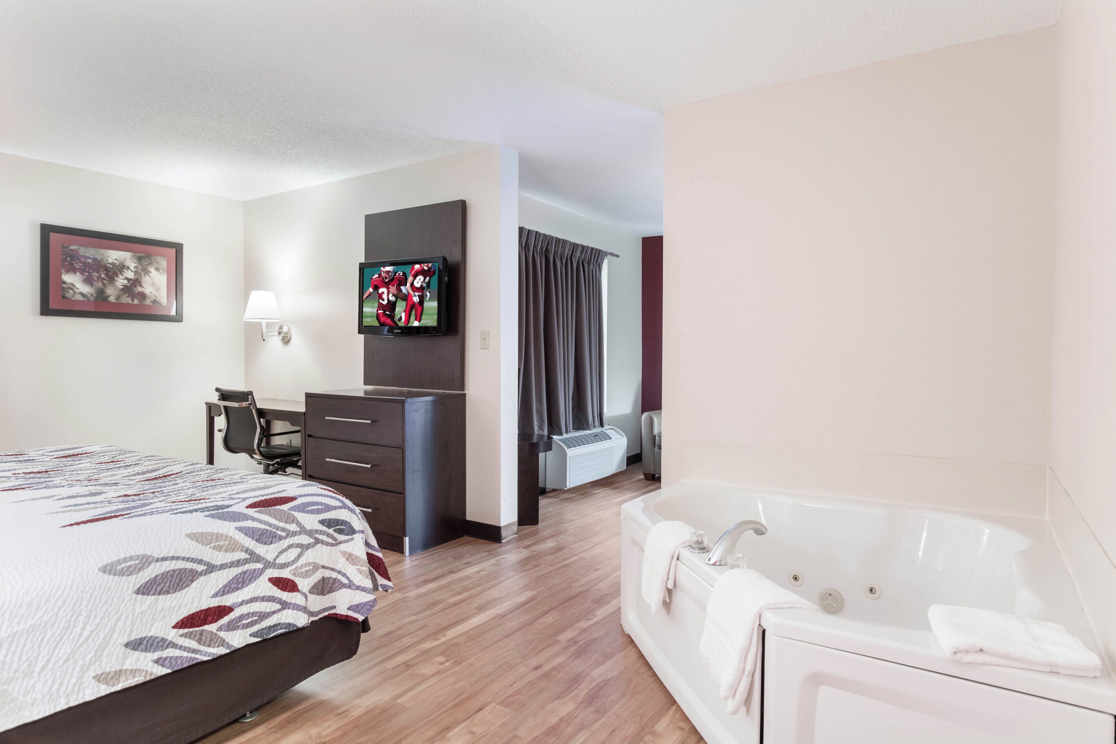 Une chambre d’hôtel comprenant un lit, un bureau, une télévision, une salle de bain avec baignoire et une fenêtre avec des rideaux.
