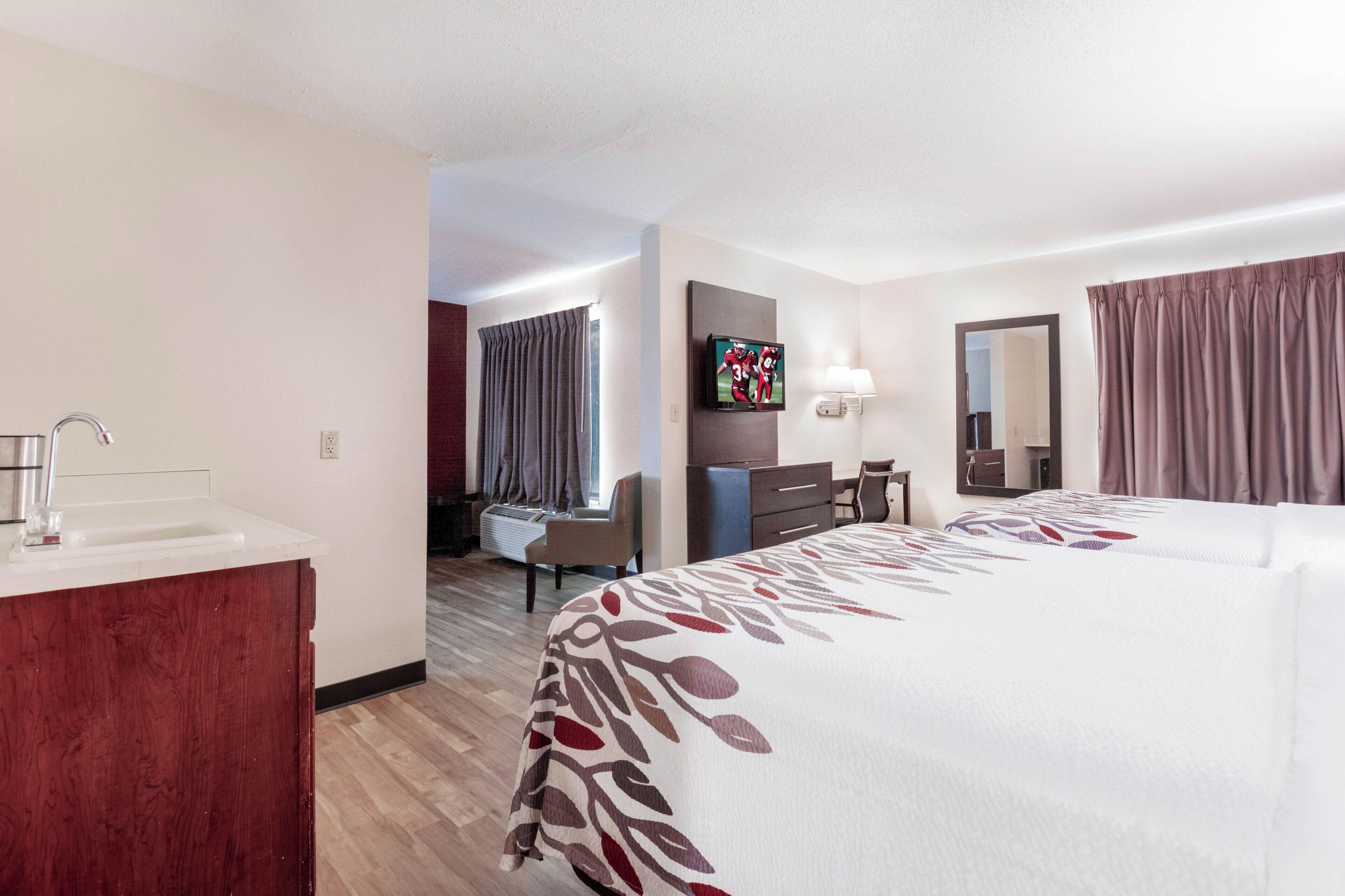 Una habitación de hotel con cama, escritorio, silla, televisor y baño.