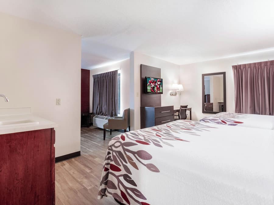 Quarto de hotel com cama, escrivaninha, cadeira, televisão e banheiro.