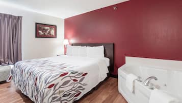 Habitación de hotel con cama, lámpara de noche, ventana grande con cortinas, un cuadro en la pared y un baño independiente con bañera.