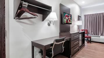 Habitación de hotel con escritorio, silla, perchero, televisor montado en la pared y una silla roja.
