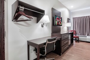Habitación de hotel con escritorio, silla, perchero, televisor montado en la pared y una silla roja.