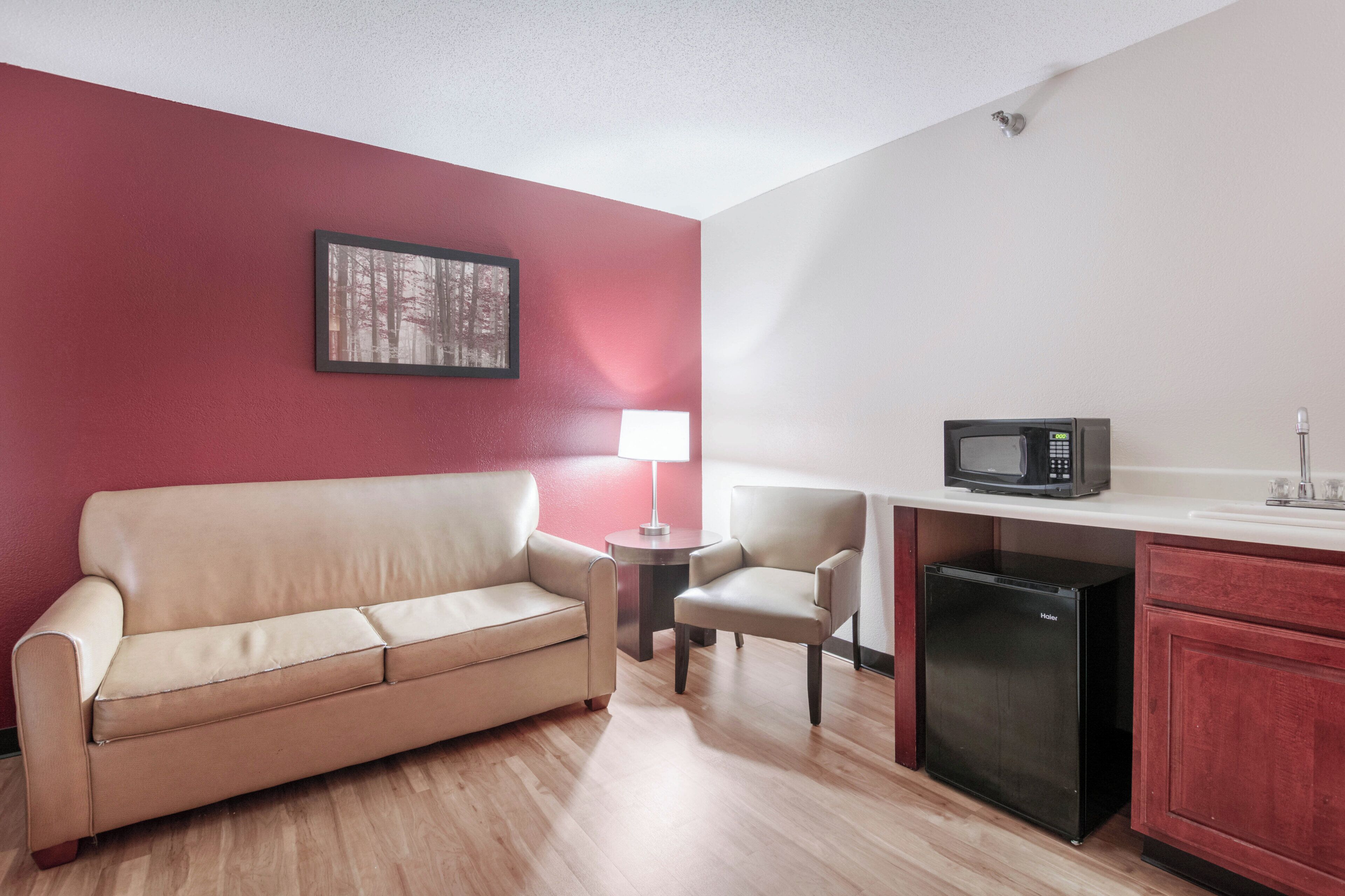 Una kitchenette compacta con microondas, refrigerador y un pequeño comedor con mesa y silla.