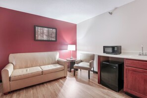 Una kitchenette compacta con microondas, refrigerador y un pequeño comedor con mesa y silla.