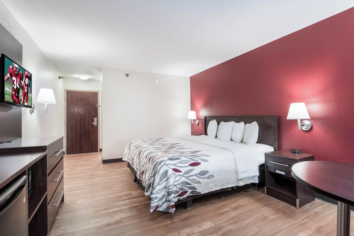 A hotel room with a bed, bedside tables, a TV, a desk, and a lamp.