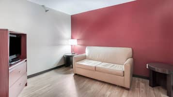 A room with a beige sofa, a TV on a wooden cabinet, a small table with a lamp, and a red accent wall.
