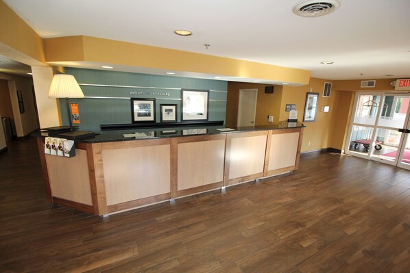 A reception desk with a wooden finish, a wall-mounted lamp, and framed pictures. - Hampton Inn Sandusky-Central (Sandusky)