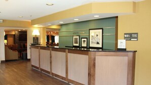 A reception desk with framed artwork, a "Manager On Duty" sign, and a "Welcome to Sandusky" sign. - Hampton Inn Sandusky-Central (Sandusky)