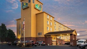 Un hotel La Quinta Inn & Suites con un letrero visible, un estacionamiento con varios coches y una entrada bien iluminada.
