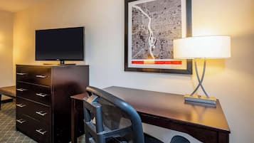 Quarto de hotel com televisão de tela plana, escrivaninha com luminária, cadeira e cômoda.