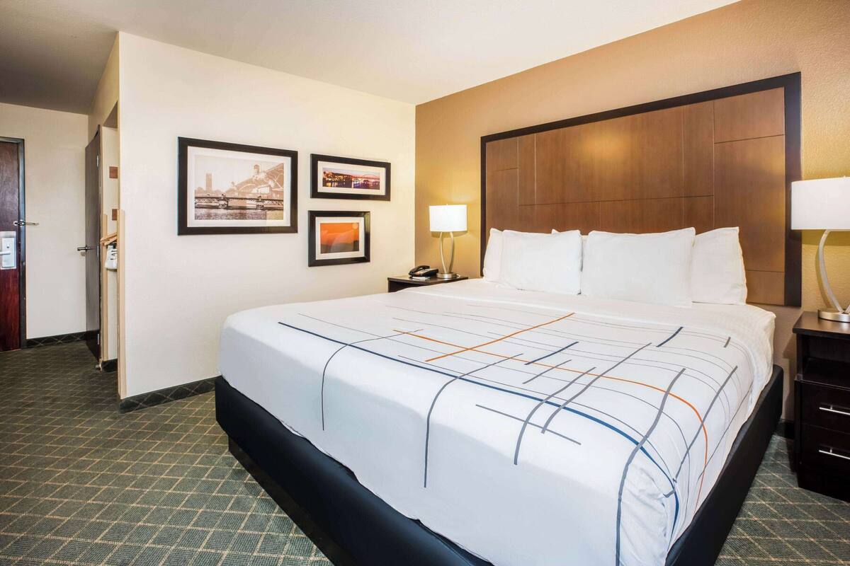 Habitación de hotel con una cama grande, cabecera de madera, mesita de noche con lámpara y cuadros en la pared.