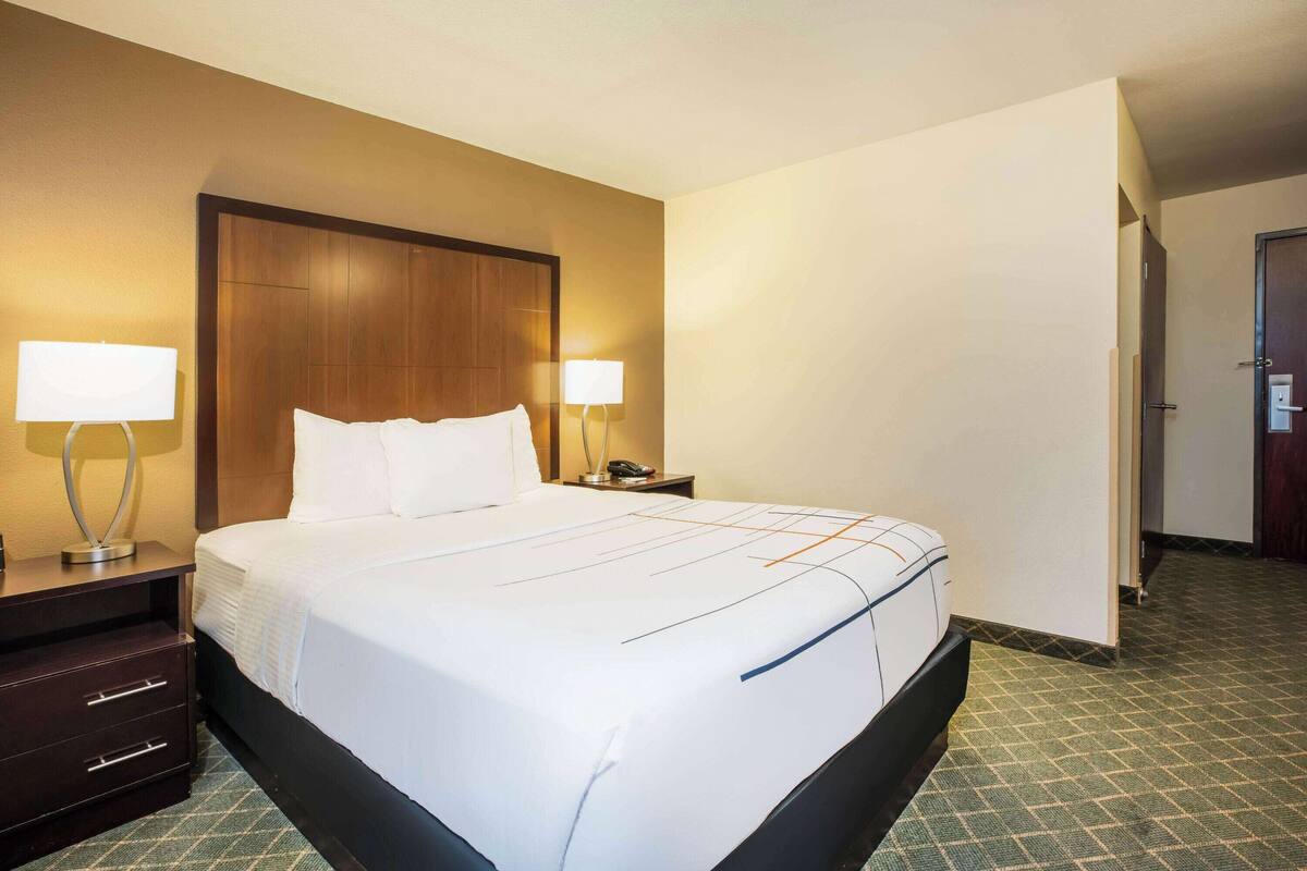 Habitación de hotel con una cama grande, dos mesitas de noche con lámparas, un cabecero de madera y piso alfombrado.