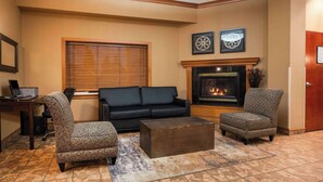 Una sala de estar con un sofá negro, dos sillones estampados, una mesa de centro de madera y una chimenea.