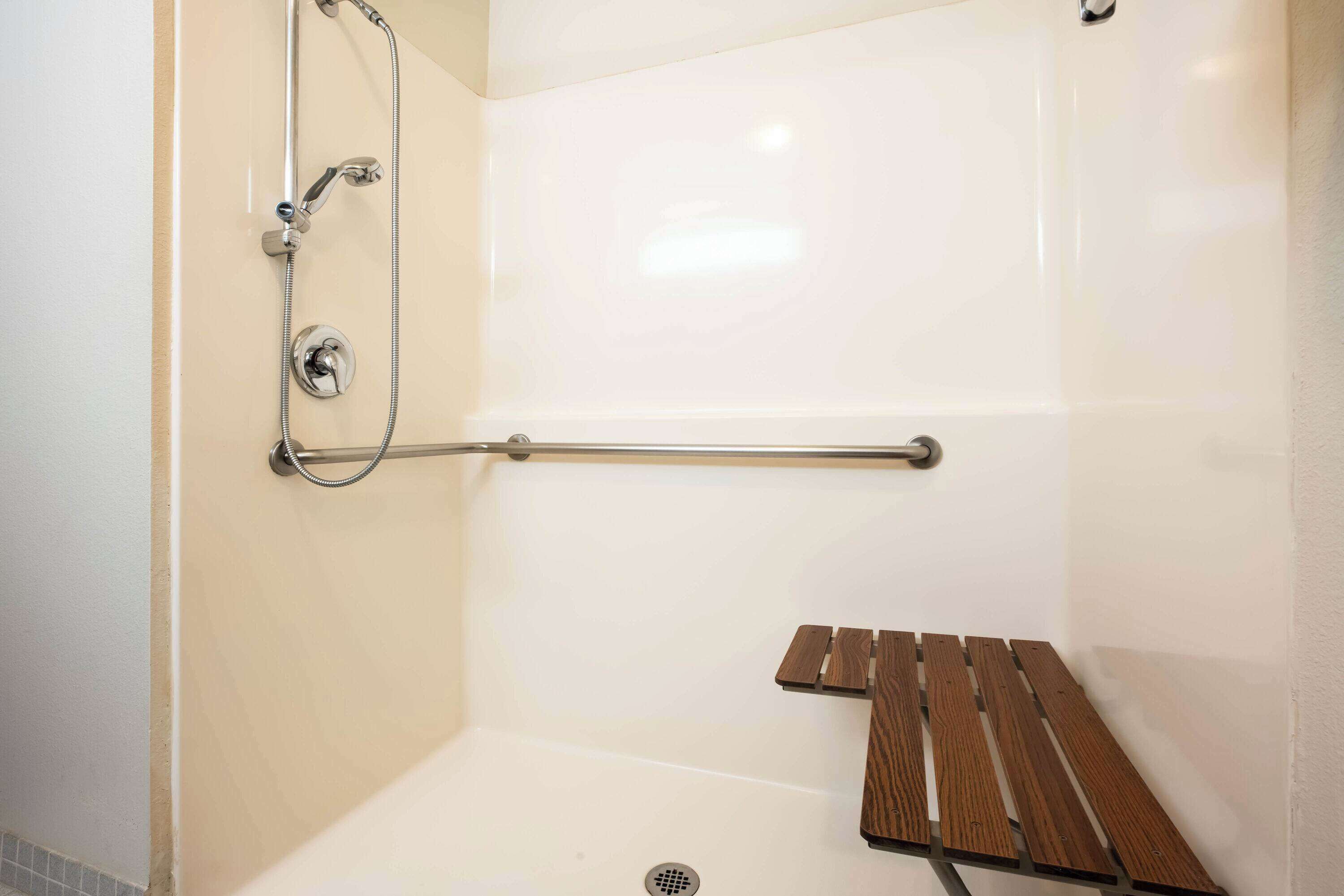 Un espace douche équipé d’une barre d’appui, d’un banc en bois et d’un pommeau de douche.