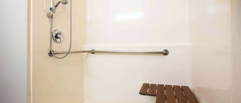 Un espace douche équipé d’une barre d’appui, d’un banc en bois et d’un pommeau de douche.