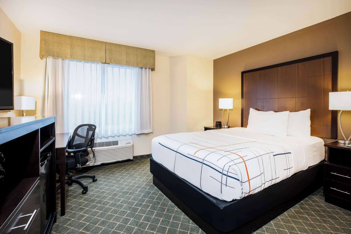 Habitación de hotel con una cama grande, un escritorio con silla, televisión de pantalla plana y ventana con cortinas.