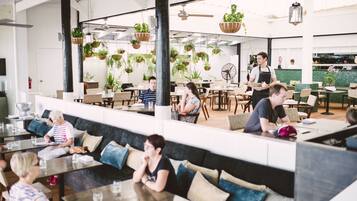 Un restaurante moderno con techos altos, plantas colgantes y una variedad de opciones de asientos, incluyendo mesas y bancos.
