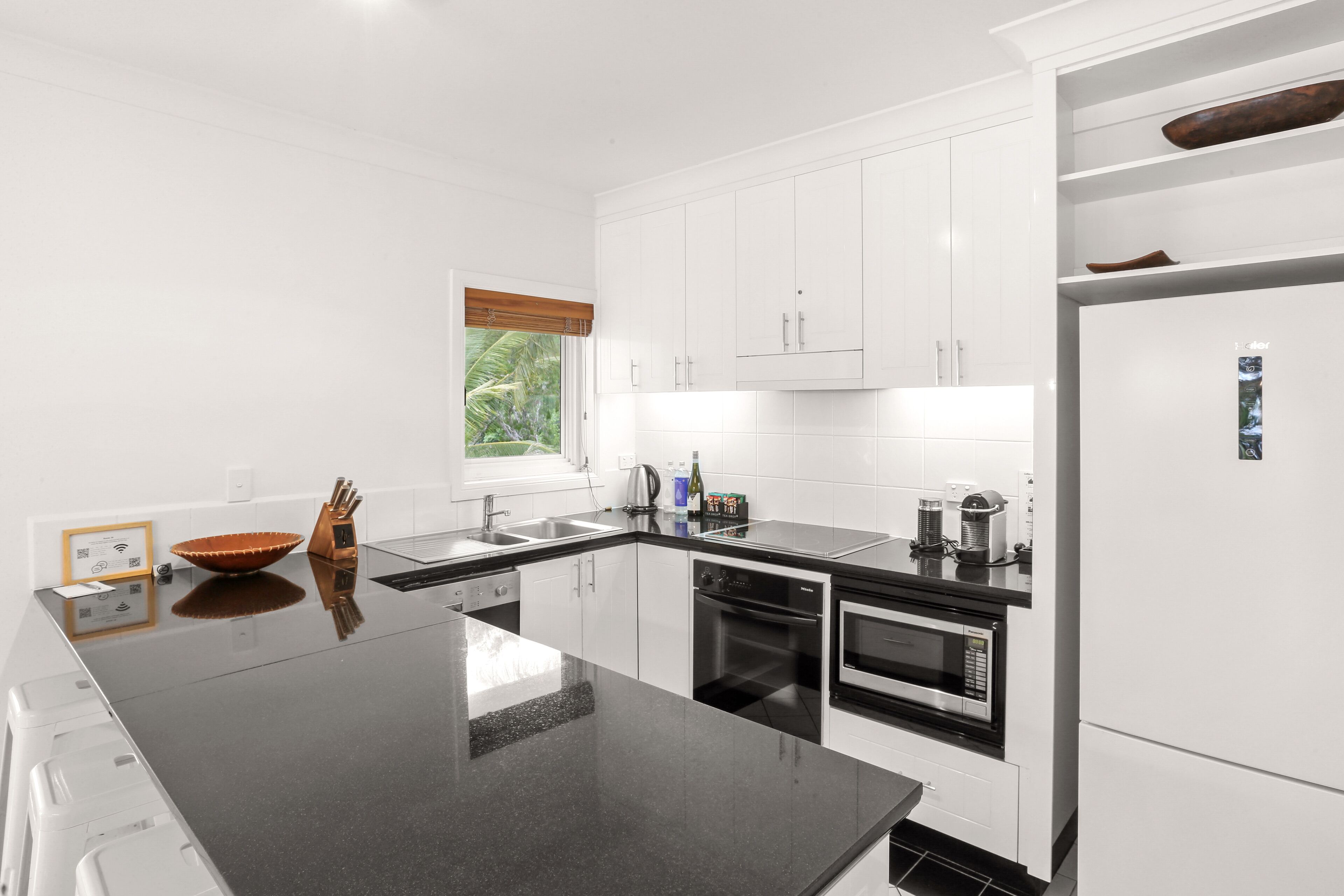 Una cocina moderna con armarios blancos, encimera negra y electrodomésticos de acero inoxidable.