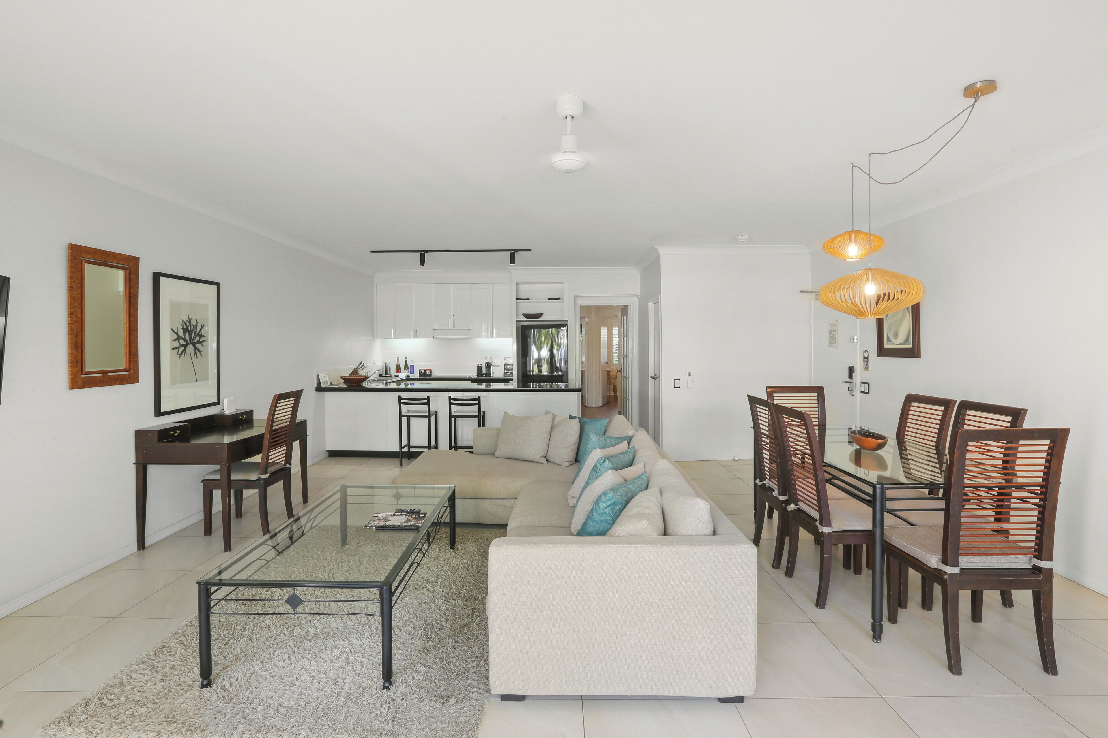 Una sala de estar moderna con sofá, mesa de comedor y sillas, una cocina al fondo y una lámpara de techo.