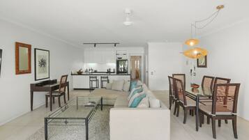 Una sala de estar moderna con sofá, mesa de comedor y sillas, una cocina al fondo y una lámpara de techo.