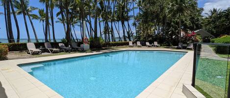 A swimming pool with tiled flooring, surrounded by palm trees and lounge chairs.