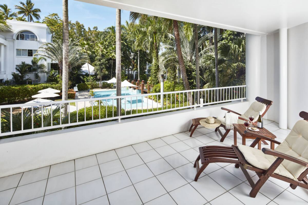 A balcony with a pool view, wooden furniture, and a white railing.