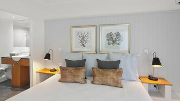 Un hotel moderno con una cama grande, dos mesitas de noche, un tocador, un aparador de madera, un baño y dos cuadros enmarcados en la pared.