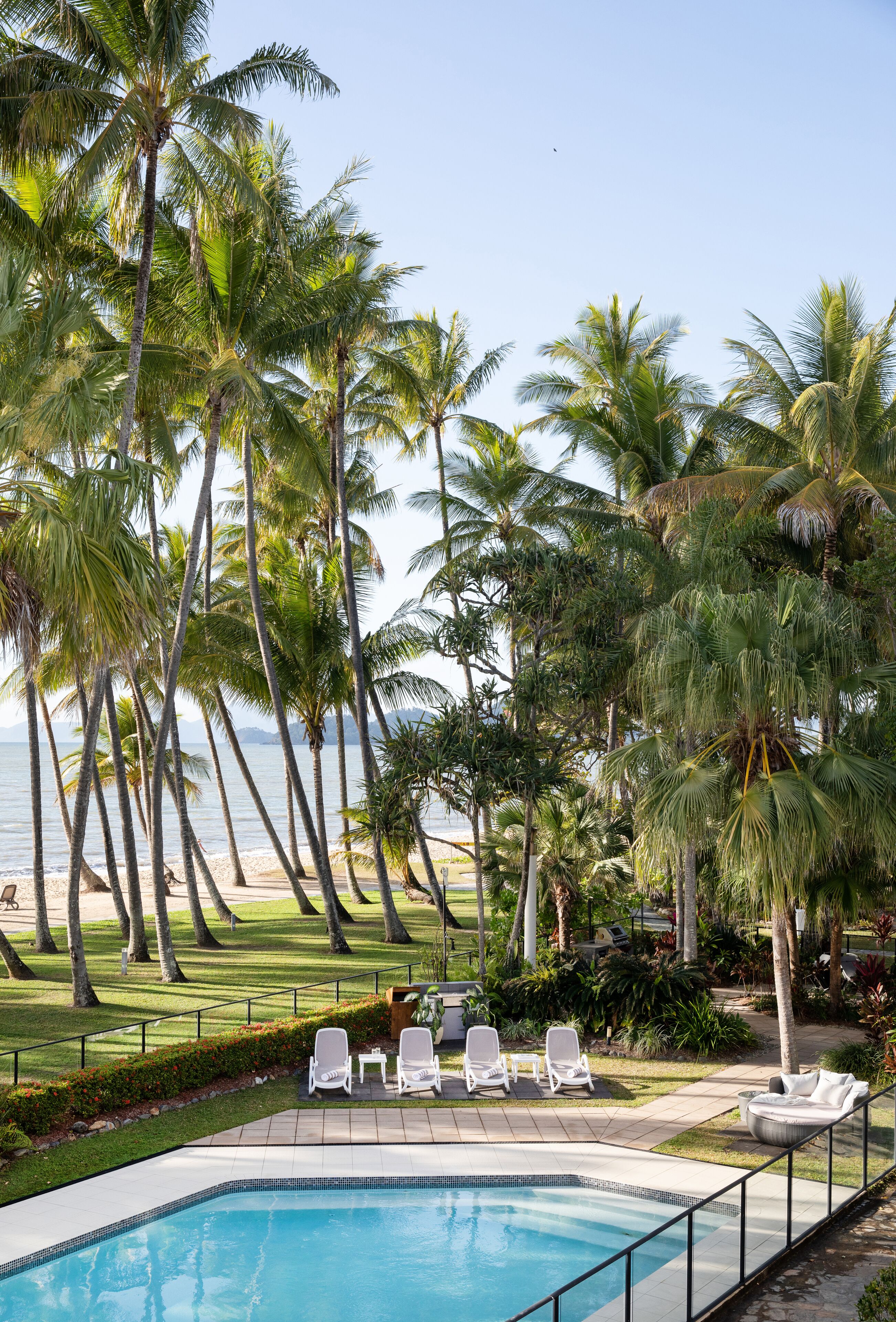 A pool area with lounge chairs, palm trees, and a view of the ocean.