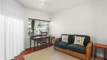 Una habitación con un sofá tejido, una mesa de madera y un ventanal con persianas.