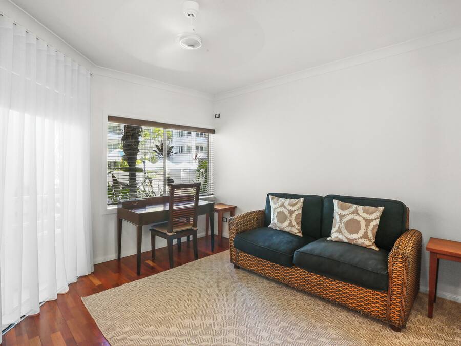 Una habitación con un sofá tejido, una mesa de madera y un ventanal con persianas.