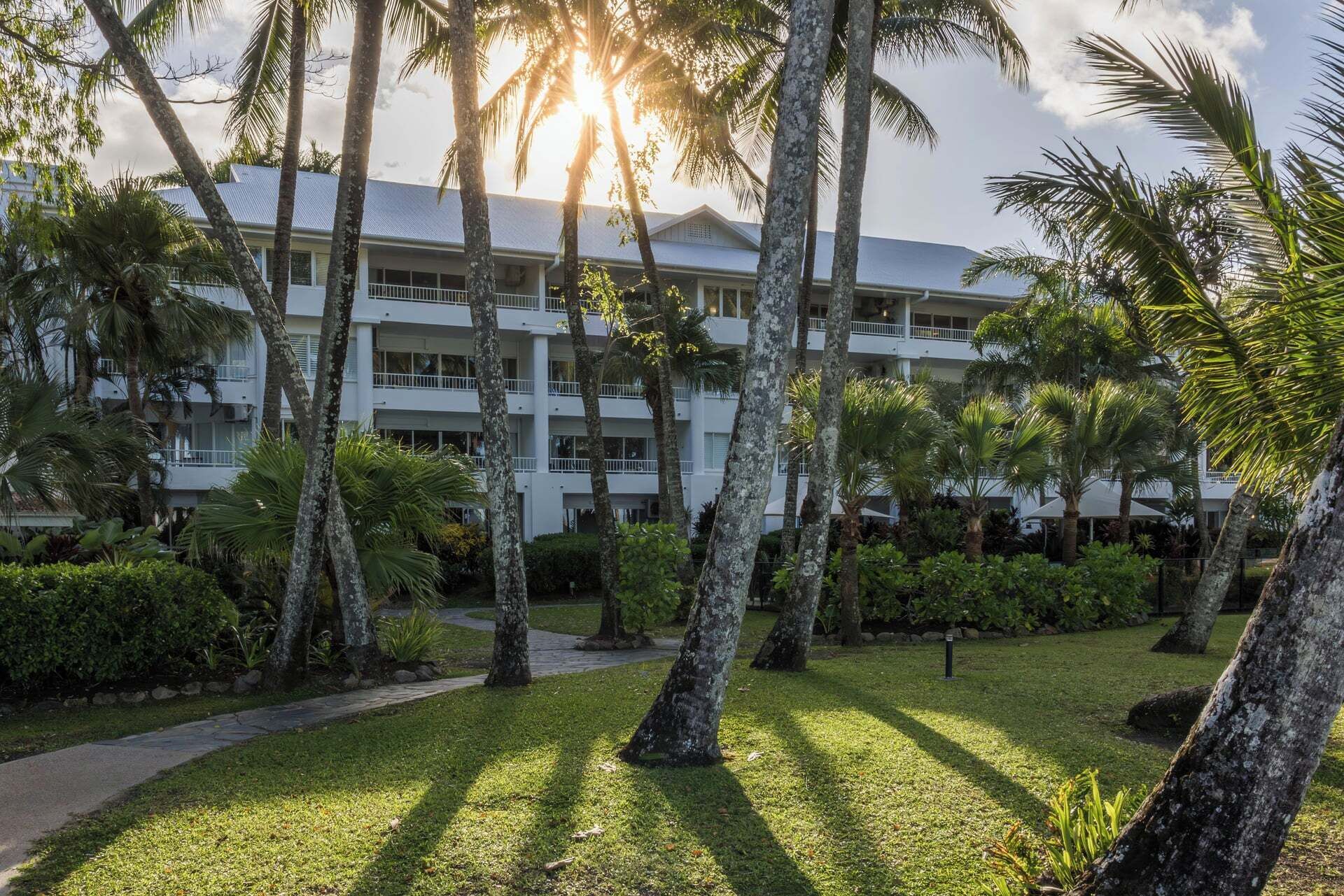A multi-story hotel with a white exterior, surrounded by palm trees and a well-maintained lawn.