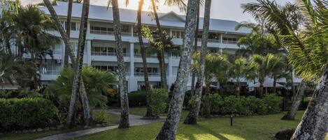 A multi-story hotel with a white exterior, surrounded by palm trees and a well-maintained lawn.