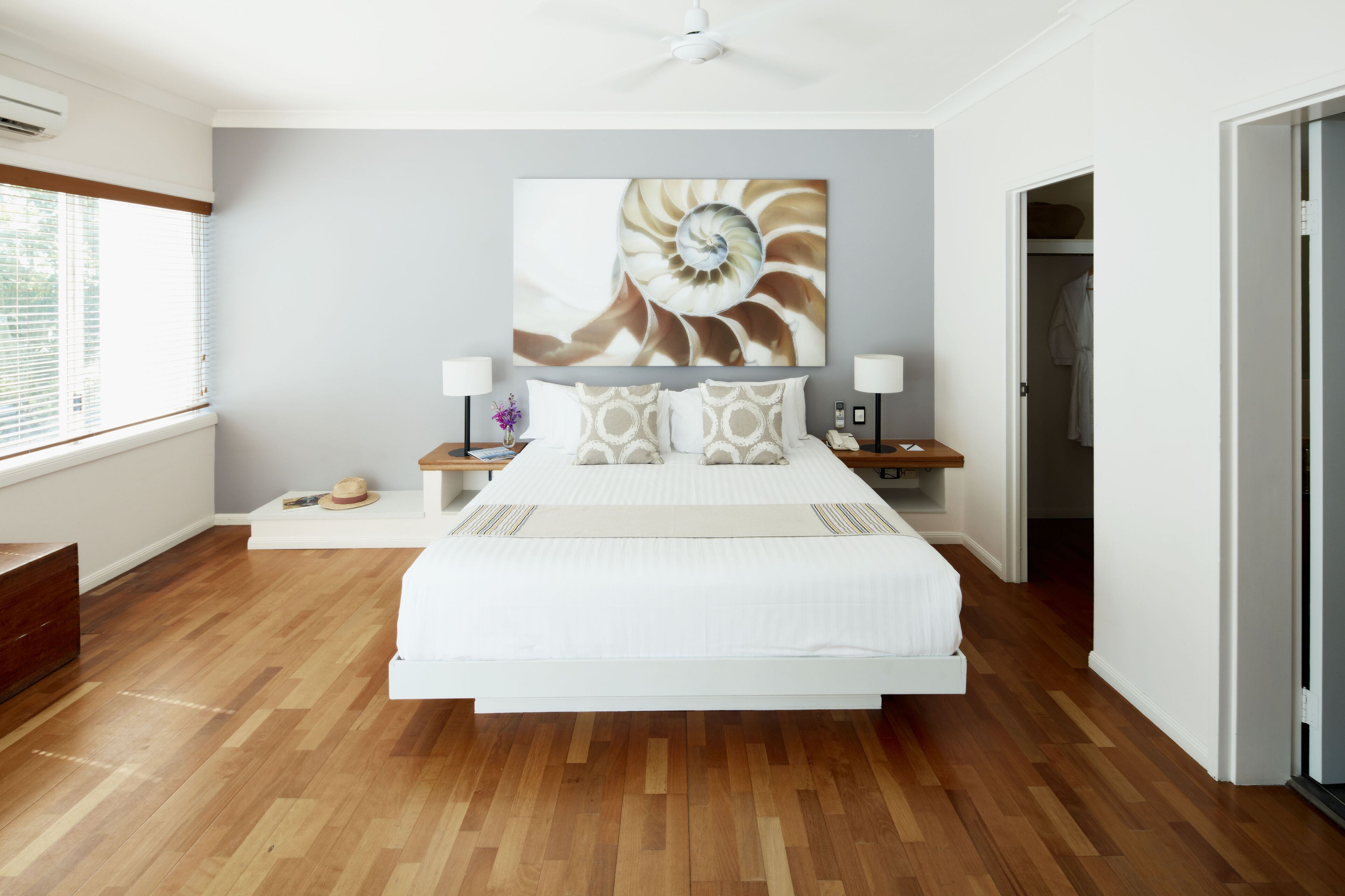 Un dormitorio moderno con una cama grande, suelo de madera, ventilador de techo y una obra de arte en la pared.
